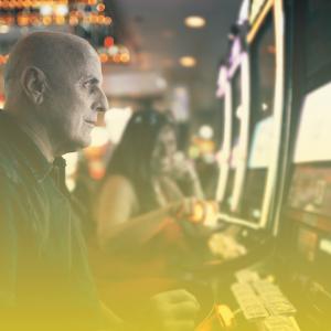 Older white man sitting at slot machine in a casino.