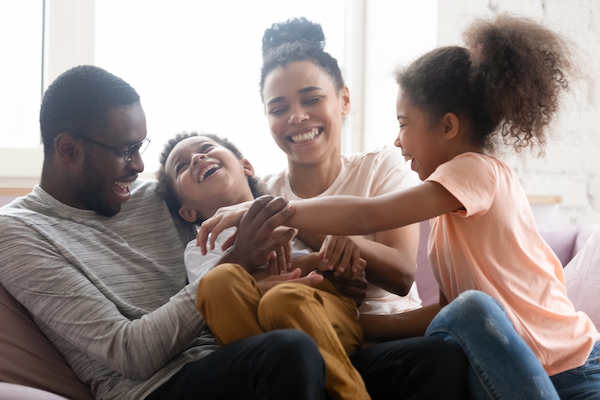 A family sits together on a cozy couch at home, all smiling and laughing, creating a warm and joyful atmosphere. Parents and children are close, sharing a happy moment filled with connection and laughter.