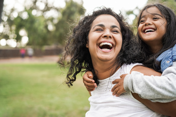 ChatGPT  A mother and daughter play together outdoors, both smiling and laughing under the open sky.