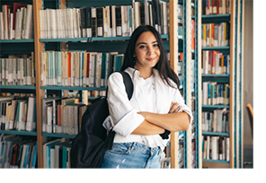 College student standing by bookcase in library.