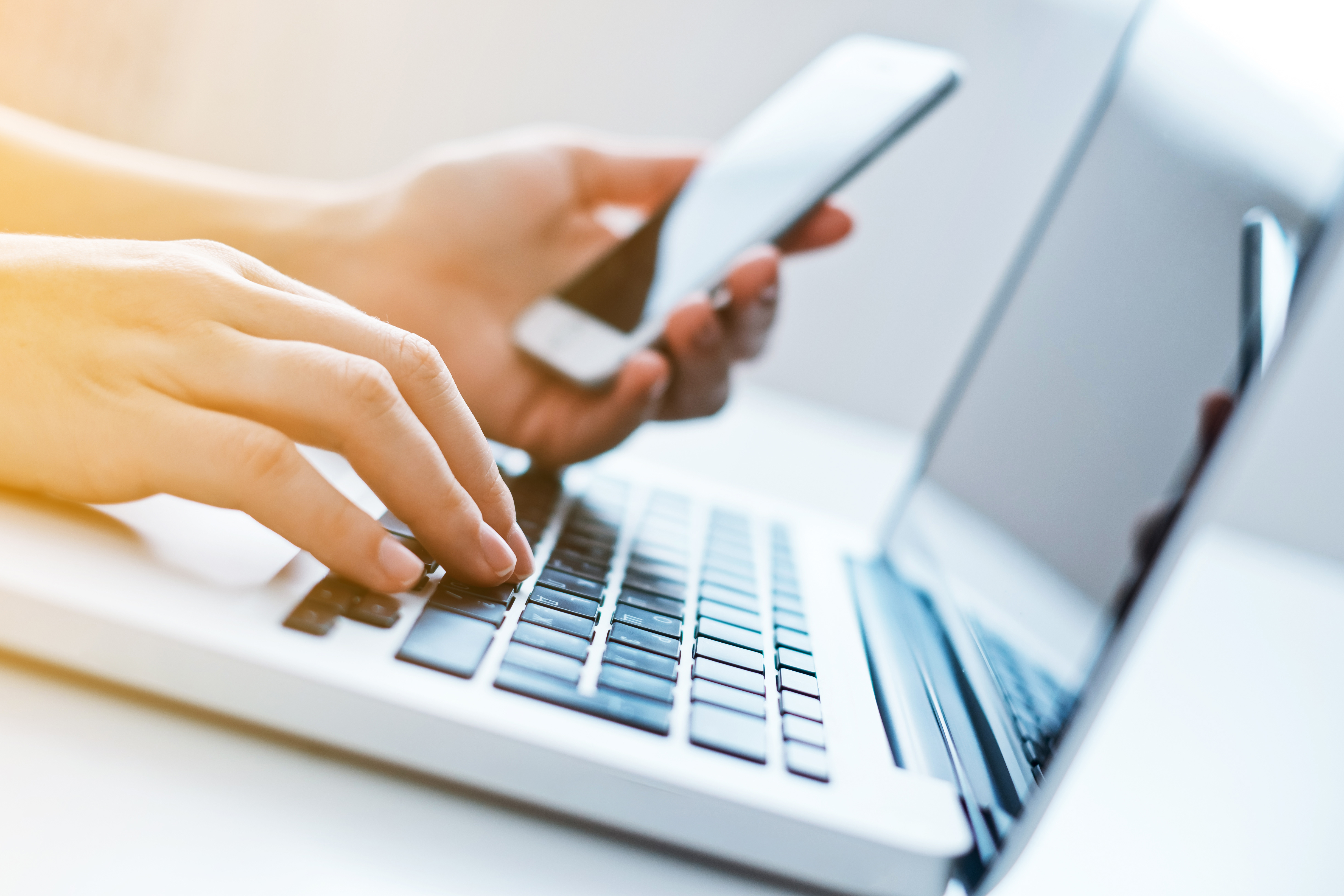 image of female hands on laptop and one hand has a smartphone