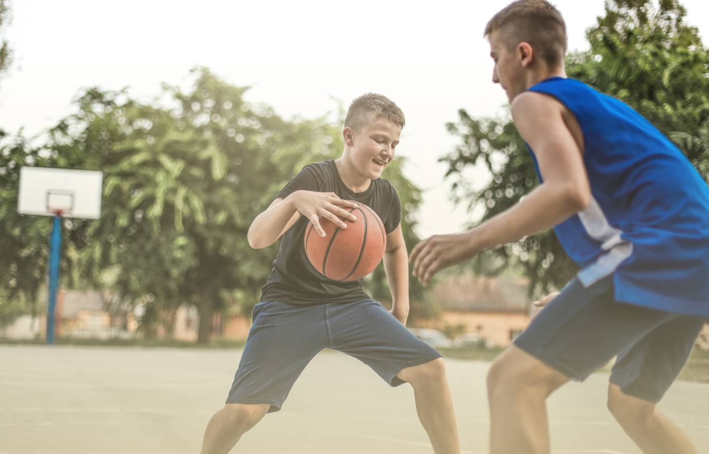 Two teen boys play basketball outside.