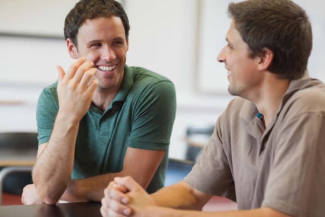 Male friends sitting indoors, chatting and enjoying a conversation in a relaxed, casual setting.