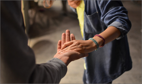 Two people holding hands, their body language a mix of concern and reassurance as they share a moment of support.