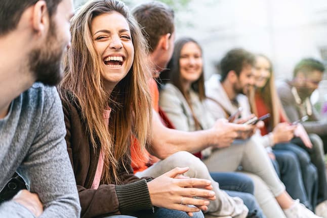 A group of teenagers sitting together on a long bench or bleacher, casually gathered and engaged with one another in a relaxed atmosphere.