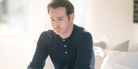 Man sitting on bed with sad facial expression