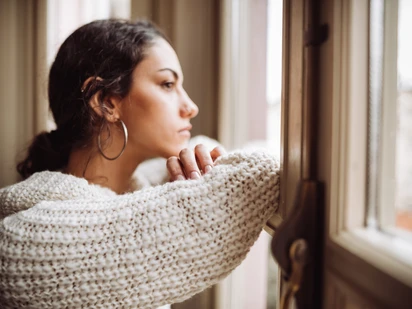 woman resting arms on window ledge looking out
