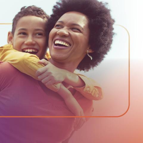 Woman smiling while supporting a toddler on her back.