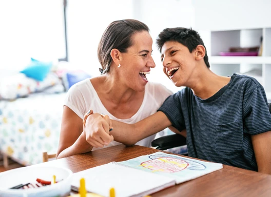 Teenager with disability and caregiver laughing