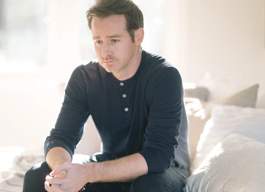Man sitting on bed with sad facial expression