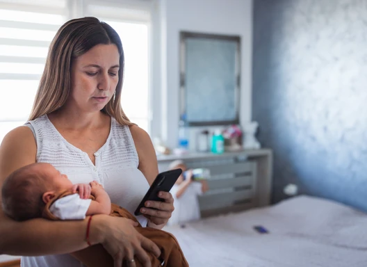 mom tired in bedroom holding newborn texting